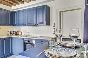 A modern kitchen with blue cabinets, stainless steel appliances, and a dining area with a table set for two. - Authentic Apartment 1br/3p - Notre Dame (Paris)
