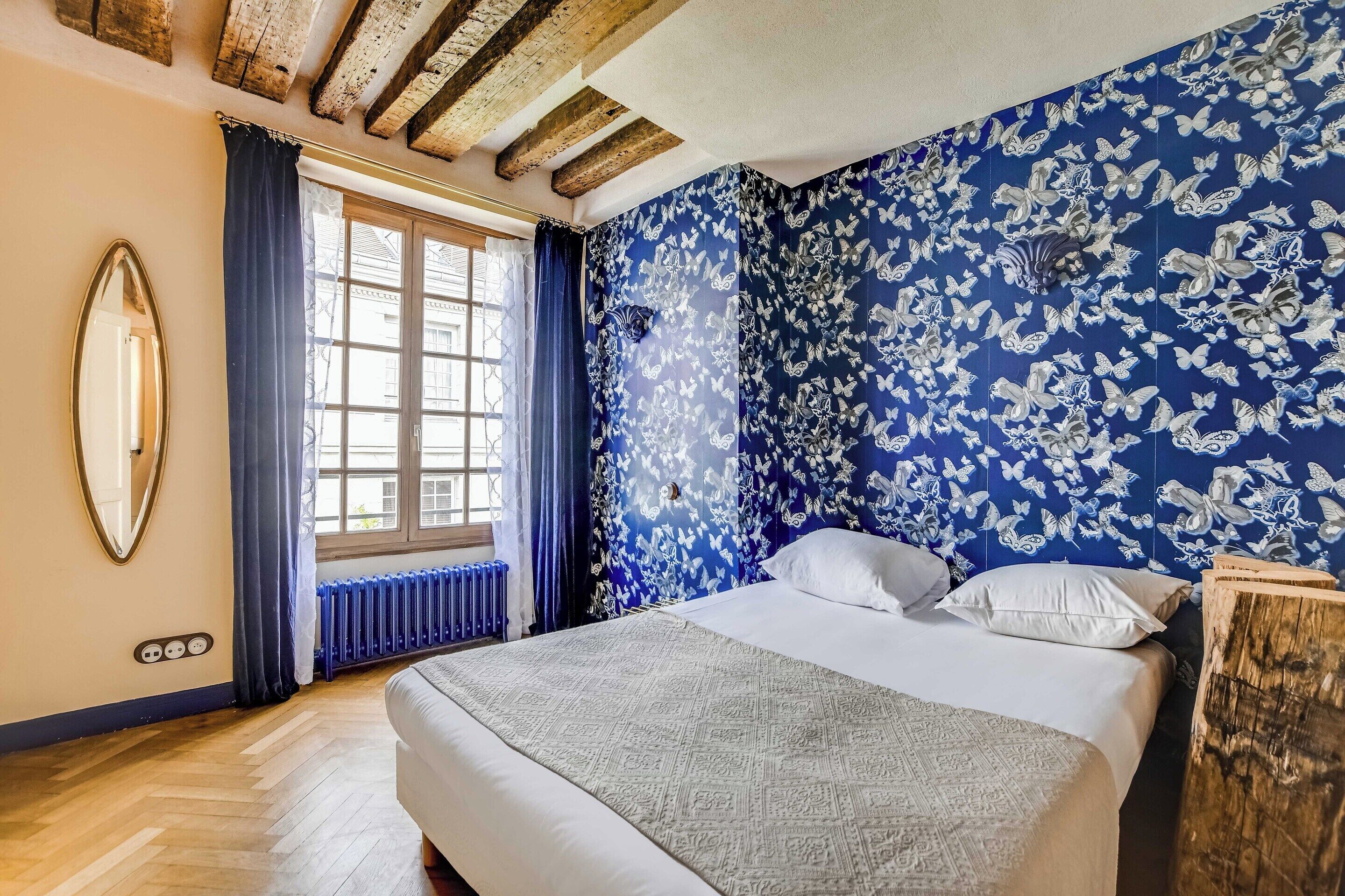 Un dormitorio con una cama grande, una ventana con cortinas, un radiador y una pared azul con estampado floral.