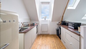 Eine schmale Küche mit Holzboden, einem weißen Kühlschrank, einer Mikrowelle und einem Fenster mit Blick.