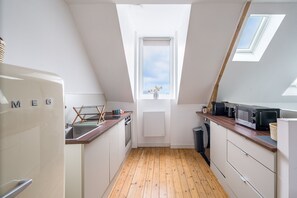 A narrow kitchen with wooden flooring, a white refrigerator, a microwave, and a window with a view. - Chez Alice - 200m de la Plage (Benodet)