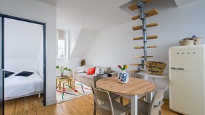 Ein modernes Zimmer mit Bett, einem Esstisch mit Stühlen, einem weißen Kühlschrank und einer loftartigen Decke mit Holzbalken.