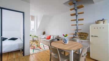 Een moderne kamer met een bed, een eettafel met stoelen, een witte koelkast en een loft-plafond met houten balken.