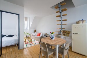 A modern room with a bed, a dining table with chairs, a white refrigerator, and a loft-style ceiling with wooden beams. - Chez Alice - 200m de la Plage (Benodet)
