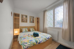 Une chambre à coucher avec un lit, une table de chevet avec une lampe, une fenêtre avec des rideaux et deux étagères fixées au mur.