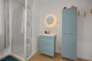 Une salle de bain avec une douche, un meuble-lavabo avec un miroir et un placard.