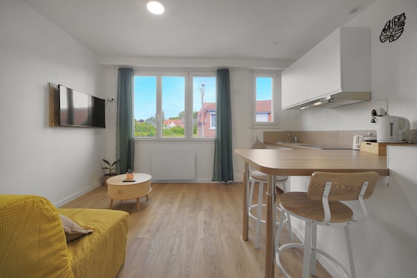 Une cuisine moderne avec un coin repas, un téléviseur fixé au mur et une vue sur l’extérieur.