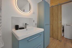 Ein modernes Badezimmer mit einem weißen Waschbecken, einem Spiegel mit Beleuchtung und einer Holztür.