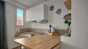 Ett modernt kök med en bänkskiva i trä, vita skåp, en inbyggd spis och ett fönster med utsikt över byggnader.