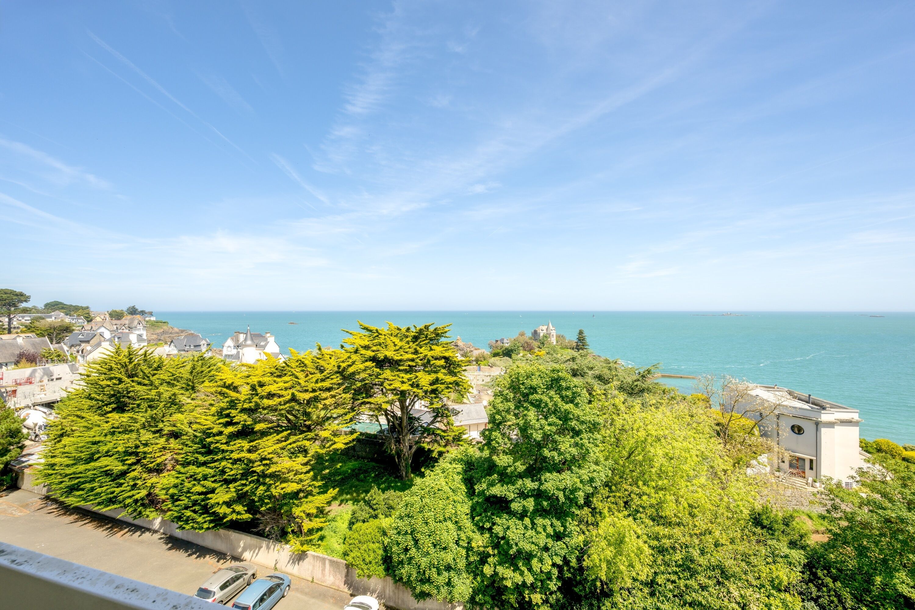 A coastal view with a white building, dense green trees, and a clear blue sky.
