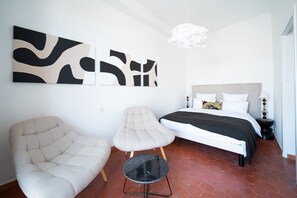 Ein Schlafzimmer mit einem Bett, zwei Stühlen, einem kleinen Tisch und abstrakter Wandkunst.