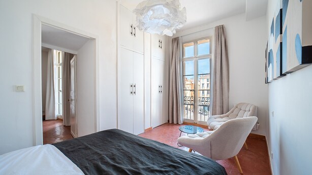 Quarto com cama, uma cadeira, uma mesa, varanda com vista e uma janela grande.