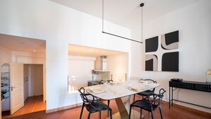 Uma cozinha moderna com armários brancos, uma mesa de jantar posta para quatro pessoas e uma pintura abstrata preta na parede.