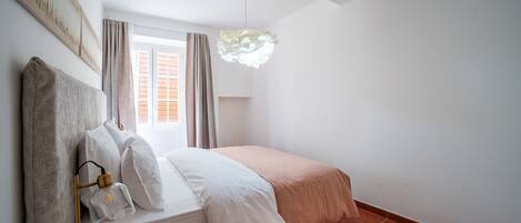 A bedroom with a bed, a bedside lamp, a window with curtains, and a wall-mounted artwork.