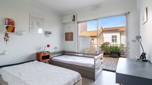 A bedroom with two beds, a desk, a window, and a view of the outside. - Escale à Canet - Au bord de la plage (Canet-en-Roussillon)