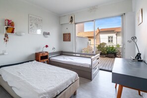 A bedroom with two beds, a desk, a window, and a view of the outside. - Escale à Canet - Au bord de la plage (Canet-en-Roussillon)