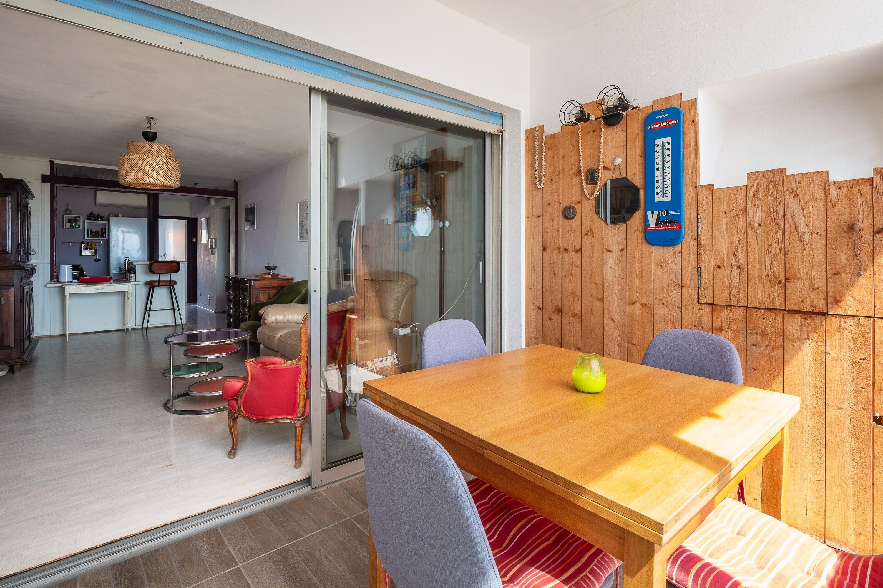 Zona pranzo con tavolo in legno, sedie e una panca. Una porta scorrevole in vetro dà accesso a una cucina.