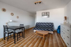 A room with a dining table, chairs, a sofa, a small wooden table, a dresser, and wall decorations. - Le Studio de Canet - À 200 m de la plage (Canet-en-Roussillon)