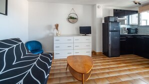 Eine moderne Küche mit Kühlschrank, Mikrowelle und Herd. Ein weißes Schranksystem mit Schubladen und ein kleiner Tisch mit Fernseher.