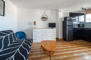 A modern kitchen with a refrigerator, microwave, and stove. There is a white cabinet with drawers and a small table with a TV. - Le Studio de Canet - À 200 m de la plage (Canet-en-Roussillon)