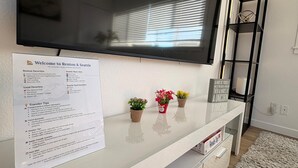 Ein modernes Wohnzimmer mit einem an der Wand befestigten Flachbildfernseher, einer weißen Unterhaltungsecke mit einem Schild und einem kleinen Regal mit Dekoration.