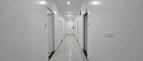 A long, narrow hallway with white walls and doors on both sides, leading to a central area.