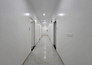 Un pasillo largo y estrecho con paredes blancas y puertas a ambos lados, que conduce a un área central.