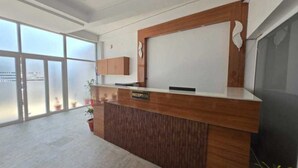 A reception desk with a 'RECEPTION' sign, large windows, and a view of the outdoors. - Deluxe Lexa Grand (Lucknow)