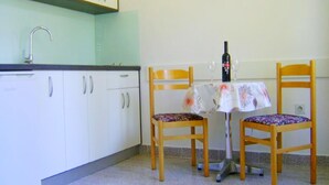 Eine kleine Küche mit weißen Schränken, einer Spüle und einem Tisch mit zwei Stühlen. Auf dem Tisch stehen eine Weinflasche und zwei Gläser.