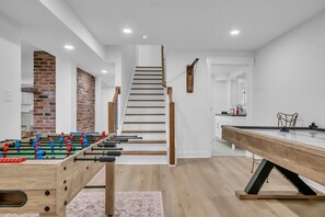 A modern interior with a foosball table, a pool table, a staircase, and a brick wall. - Evergreen Cottage Escape (Pegram)