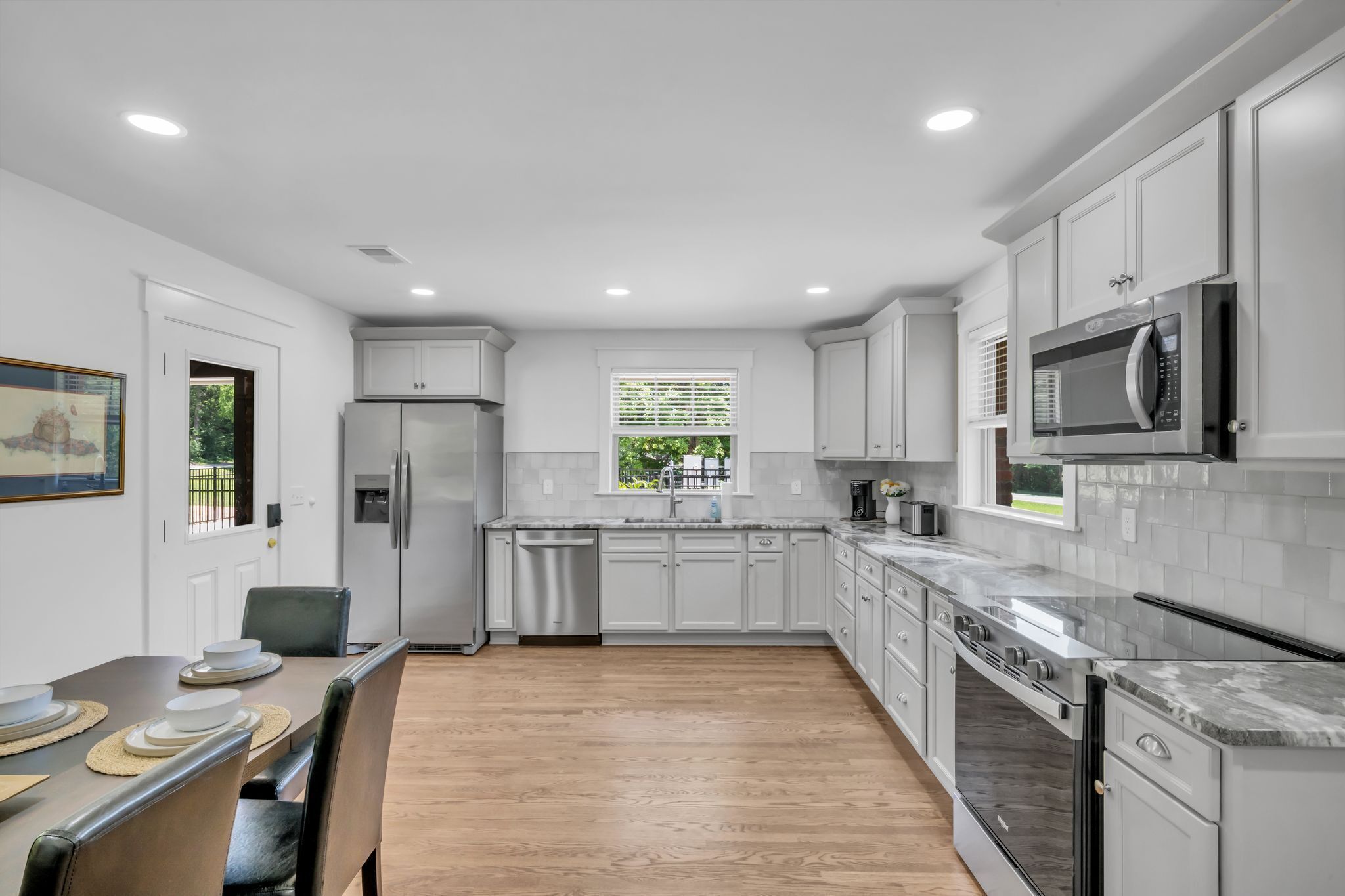 A modern kitchen with white cabinets, stainless steel appliances, and a wooden floor.