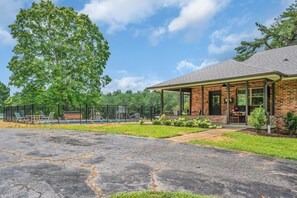 A brick building with a covered patio area, a fenced outdoor seating area, and a paved driveway. - Evergreen Cottage Escape (Pegram)