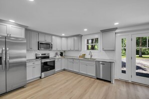 A modern kitchen with white cabinets, stainless steel appliances, and a view of the outdoors. - Evergreen Cottage Escape (Pegram)