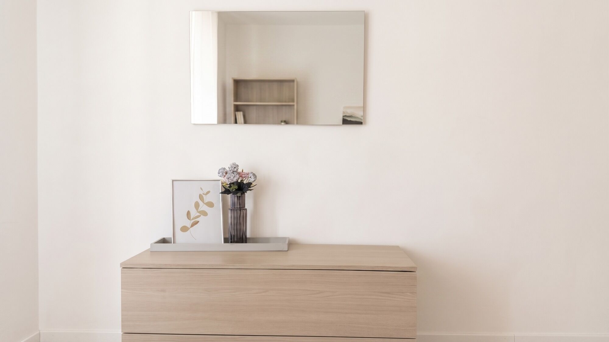 Une pièce au décor minimaliste, avec une commode en bois, une œuvre d’art encadrée et un vase rempli de fleurs.