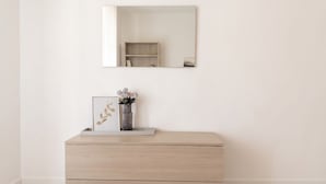 Een minimalistisch ingerichte kamer met een houten dressoir, een kunstwerk in een lijst en een vaas met bloemen.