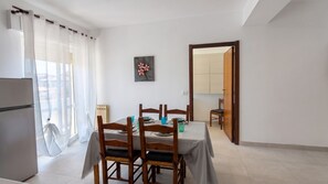 A dining area with a table set for four, a refrigerator, and a view of a balcony. - Urban Nest Alghero - Two Bedroom Apartment, Sleeps 5 (Alghero)
