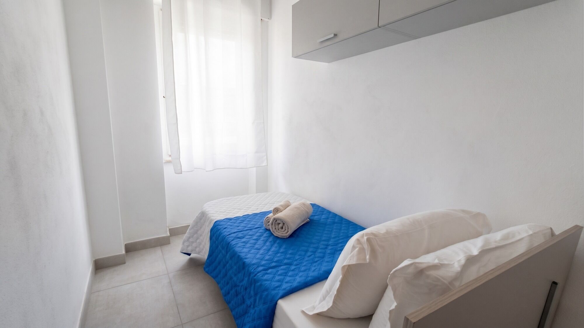 Une petite pièce propre, avec un lit, une fenêtre avec des rideaux et un mur blanc.