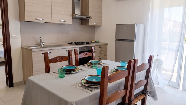 Een moderne keuken met houten kastjes, een eettafel gedekt met borden en glazen, en een koelkast.
