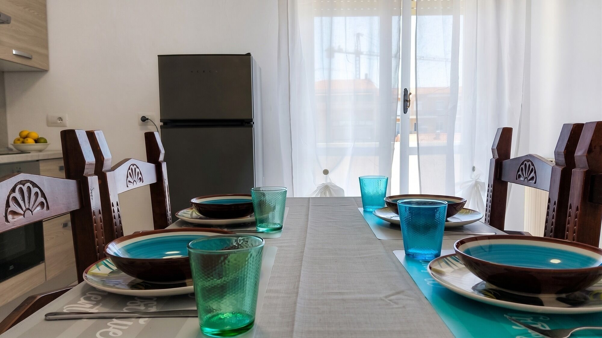 A dining table set with plates, bowls, and glasses, with chairs that have a decorative backrest.