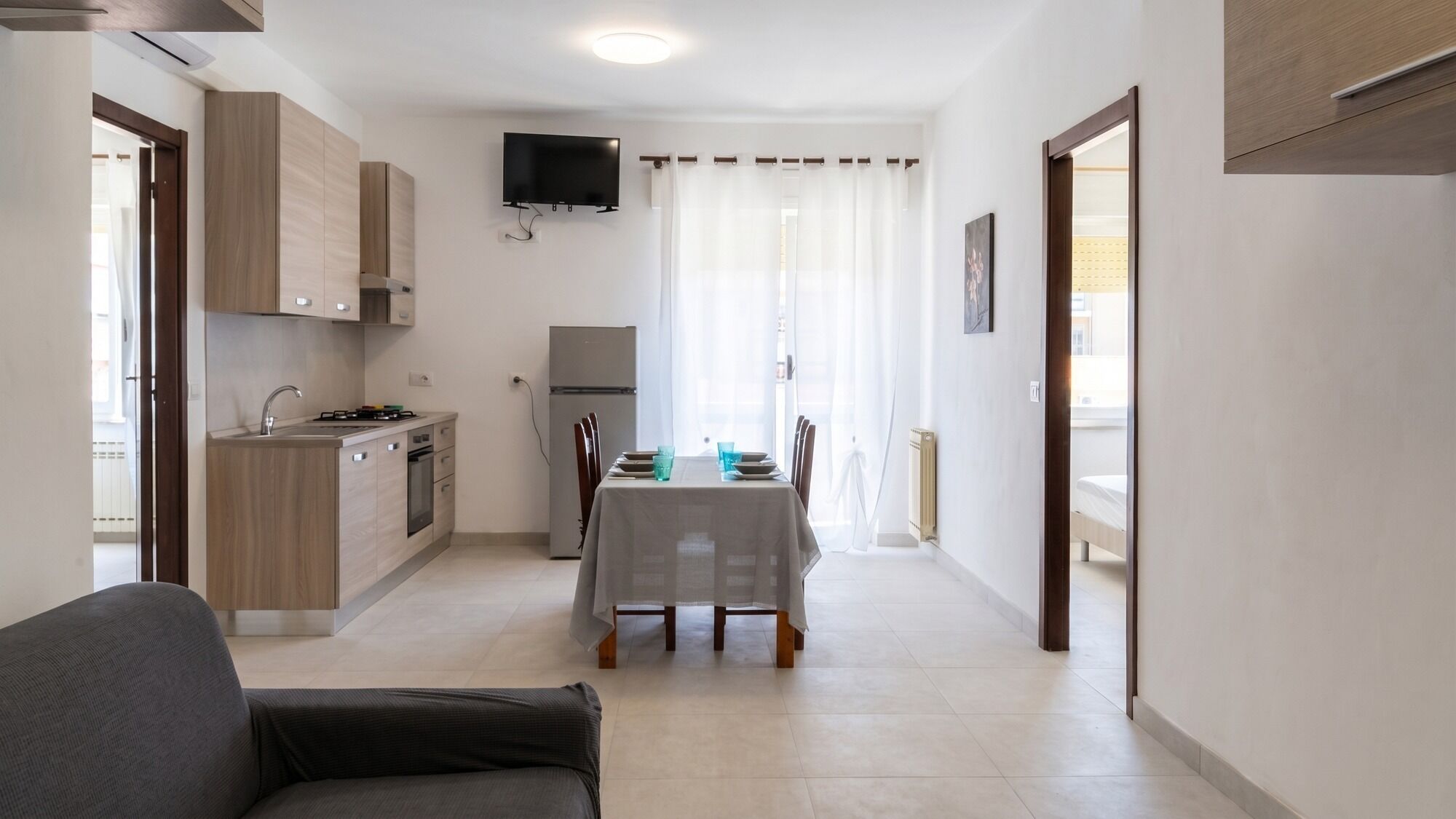 A compact kitchen with a dining area, a flat-screen TV mounted above the counter, and a table set for two.