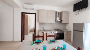 A modern kitchen with a dining table set for four, a built-in oven, and a refrigerator. - Urban Nest Alghero - Two Bedroom Apartment, Sleeps 5 (Alghero)