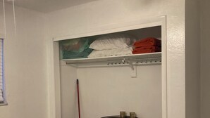 Una habitació amb ventilador de sostre, un llit, un moble d'emmagatzematge amb un bótes decoratiu i una estant amb tovalloles doblades.