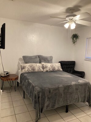 A bedroom with a bed, a ceiling fan, a small table, and a potted plant. - Great Location-4 mil 5th Ave & 1 mil Beaches-Entire Condo w/ Modern design (Naples)