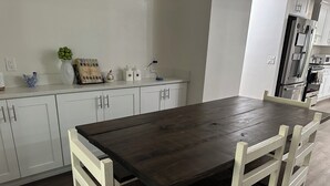 A modern kitchen with white cabinets, a dark wooden table, and white chairs.