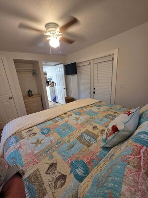 Ein Schlafzimmer mit einem Bett, einem Deckenventilator, einem an der Wand montierten Fernseher und einem Kleiderschrank mit Schiebetüren.