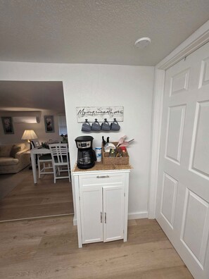 Eine kleine Küche mit Kaffeemaschine, einer Korb voller Gegenstände und einem an der Wand befestigten Schild.