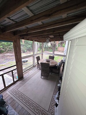 Eine überdachte Terrasse mit rundem Tisch, Korbstühlen, großen Fenstern und einer Holzbeschichtung.