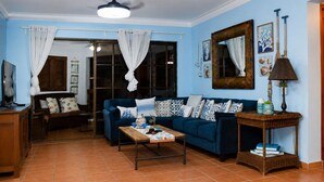 Una sala de estar con un sofá azul, una mesa de centro, una mesita de mimbre y un ventilador de techo.