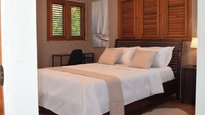 Un dormitorio con cama, escritorio, silla, lámpara y un cuadro en la pared.