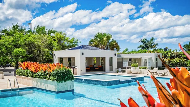 Une piscine à l’eau d’un bleu cristallin, entourée de bâtiments blancs et d’une végétation luxuriante.