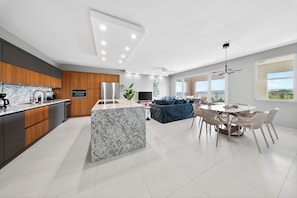 Una cocina moderna con una isla de mármol, armarios de madera y un comedor con una mesa redonda y sillas.